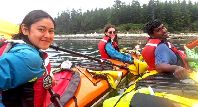 Three people wearing life jackets sit inside colorful kayaks on calm water and smile for the photo.